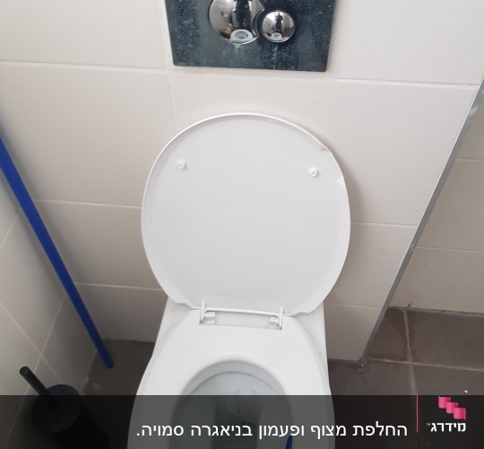 אסלה עם מכסה פתוח ולחצן הדחה על הקיר
